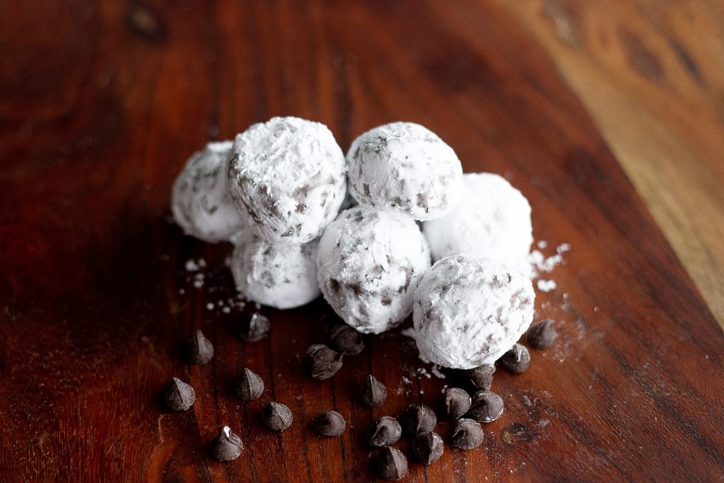 Powdered sugar-covered chocolate truffles with scattered coffee beans on a dark wooden surface.