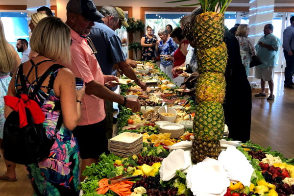 People are at a buffet table filled with various dishes, decorated with pineapples and surrounded by a wooden interior. This holiday catering setup is designed to wow your guests with its vibrant presentation and diverse menu ideas.